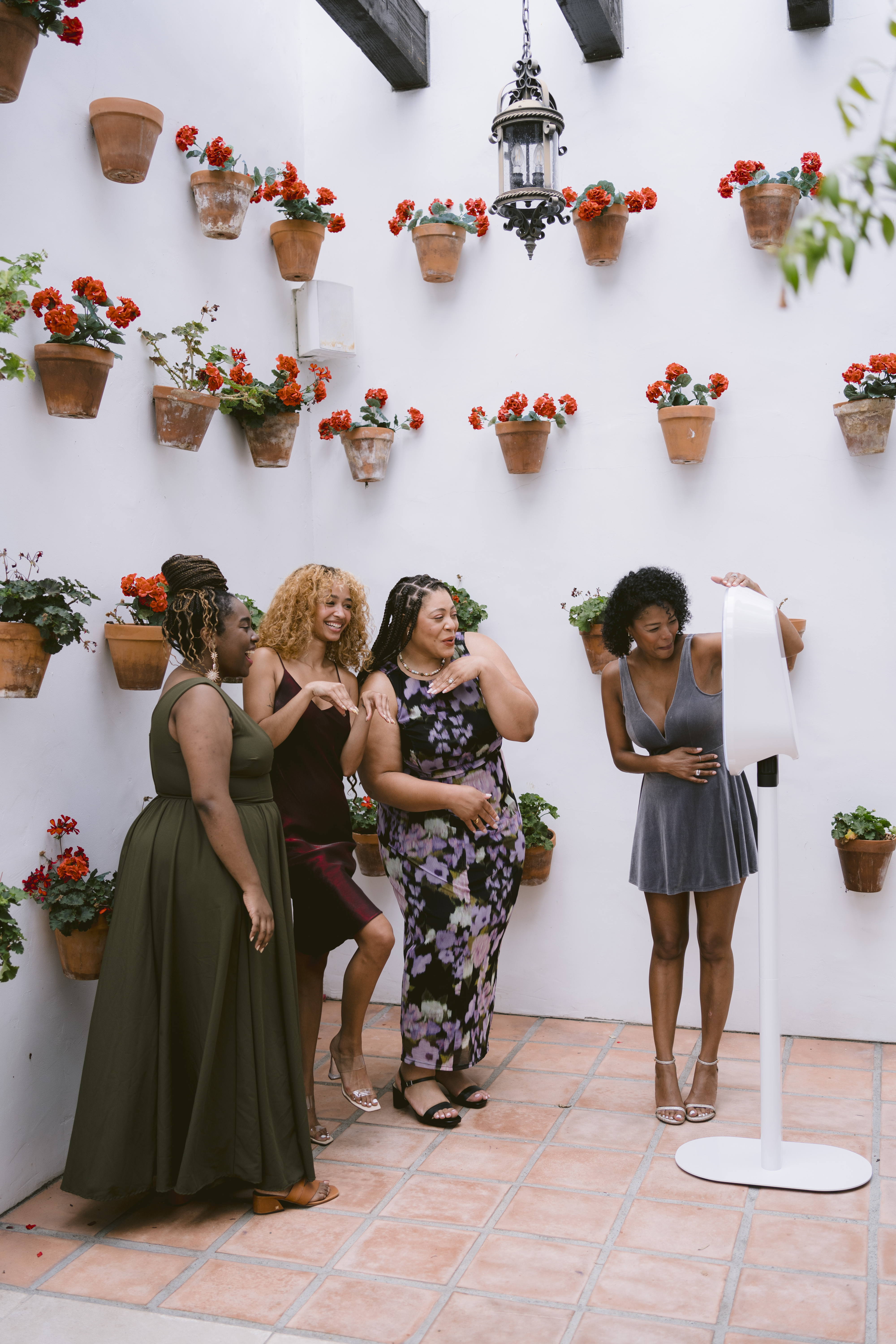 Four women taking fun photos with a modern EverGlow Booth in an outdoor courtyard with potted red flowers.