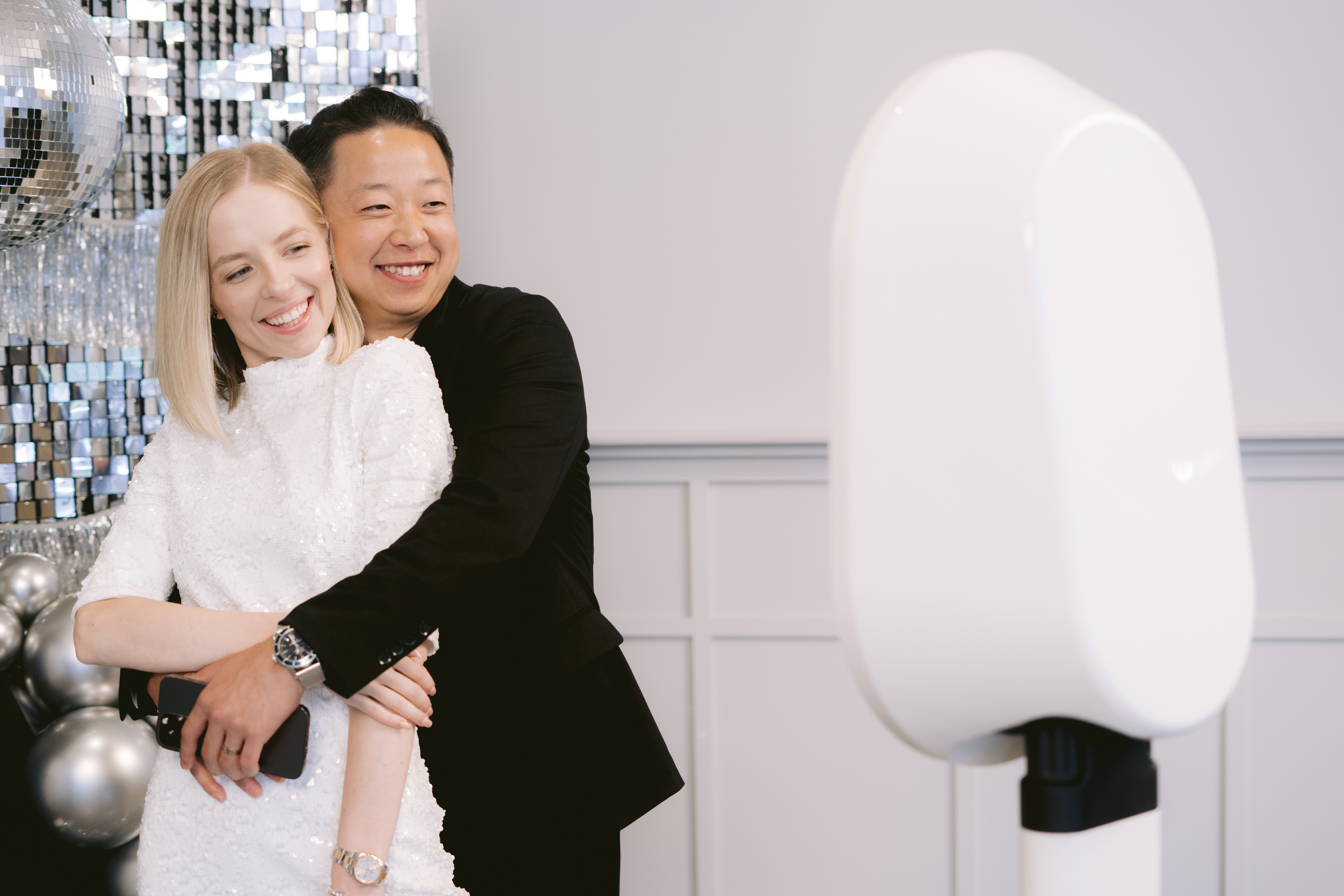 Smiling couple embracing while posing for a photo booth picture at a lively event with a disco ball backdrop.
